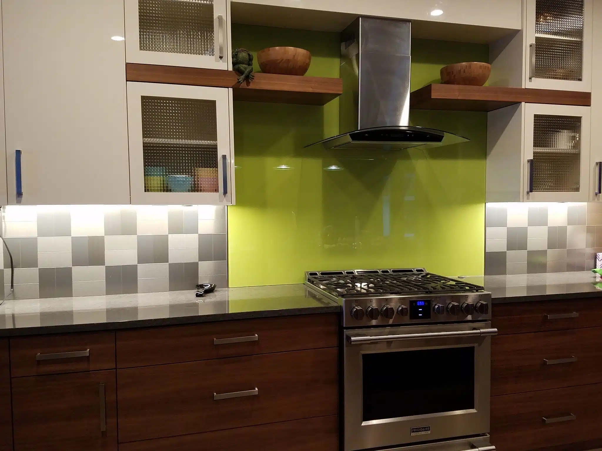 A modern kitchen featuring a gas range oven against a vibrant lime green glass backsplash.